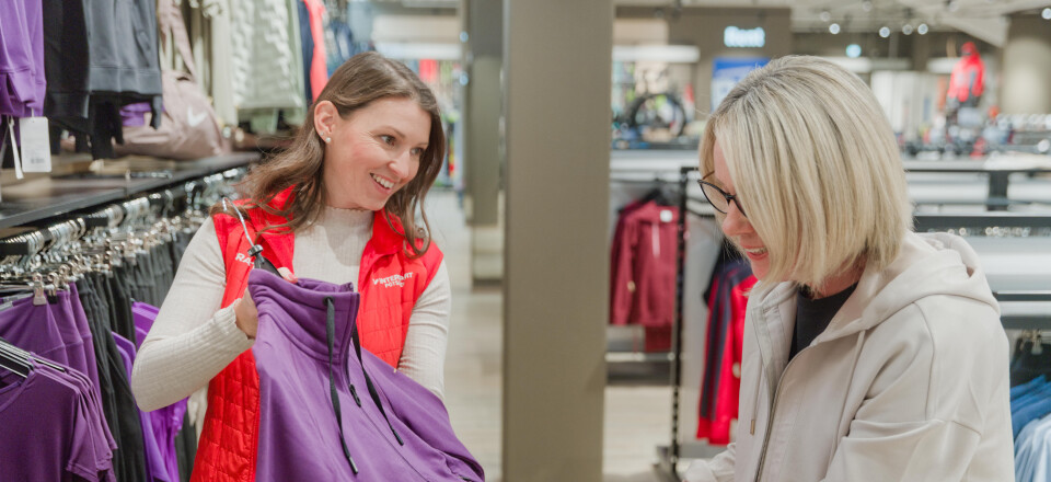 Frau kauft lila Sportbekleidung mit Verkäuferin in einem Bekleidungsgeschäft.