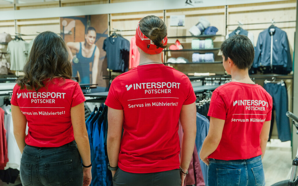 Zaměstnanci Intersportu v červených tričkách ve sportovním obchodě, prezentující sportovní oblečení a maloobchodní prostředí.