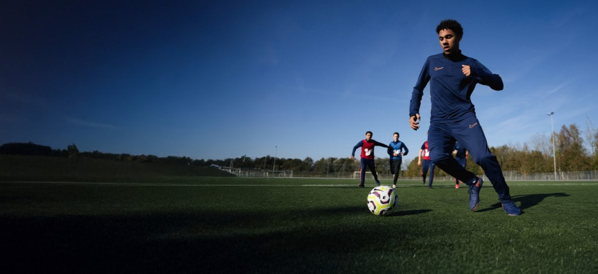 Fußballspieler dribbelt einen Ball auf einem grünen Feld während einer Trainingseinheit mit Teamkollegen.