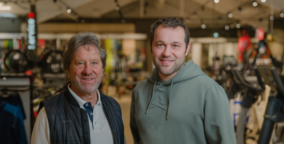 A family is preparing for skiing indoors. The smiling child in orange is fitted with a helmet by a person in blue. The setting is bright and warm.
