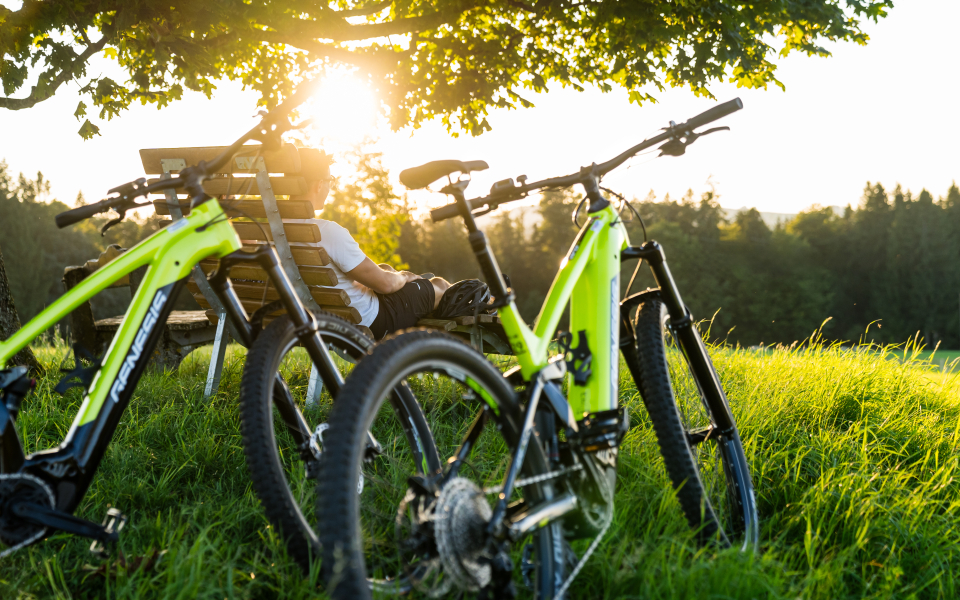 Zwei Fahrräder stehen auf einer Wiese, im Hintergrund ist eine tiefstehende Sonne zu sehen.