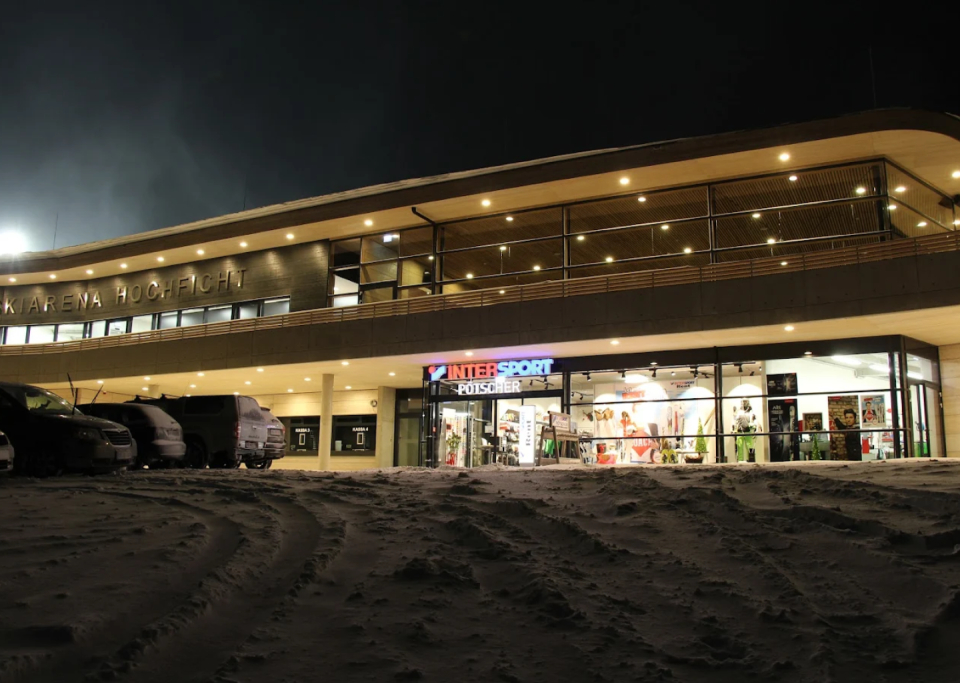 Intersport store facade at night in snowy landscape, featuring winter sports equipment and car tracks.