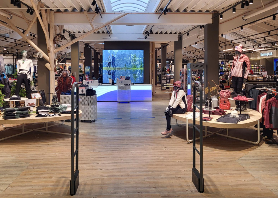 Interior of outdoor clothing store featuring mannequins, wood displays, and nature scene video wall.